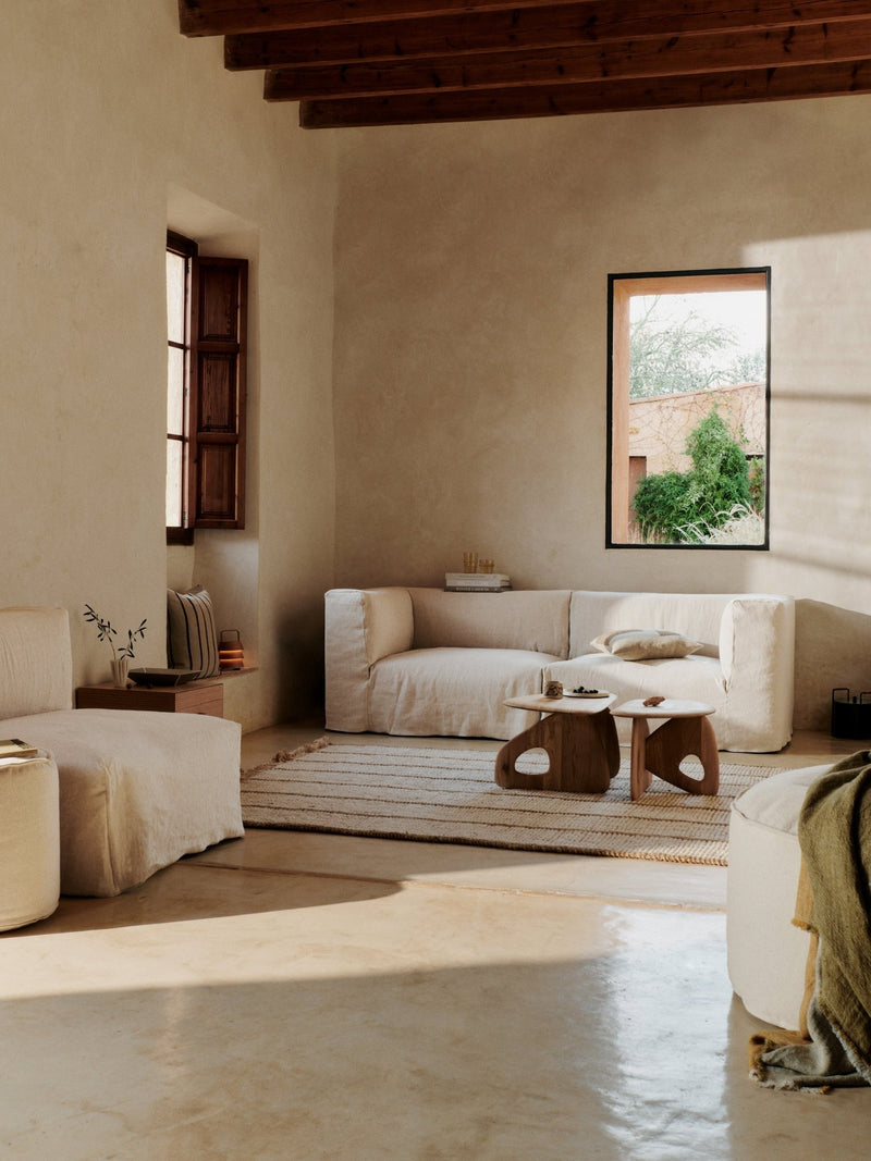 A minimalist beige chair with a rounded cushion and short legs.