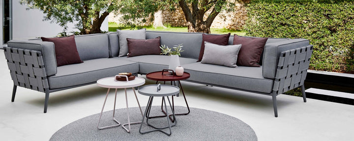Modern conic sectional sofa in gray fabric with decorative cushions, accompanied by stylish side tables and a round rug.