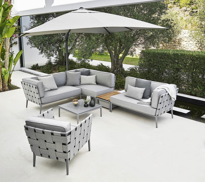 Stylish outdoor seating arrangement featuring a grey sectional sofa, armchair, and coffee table under a large umbrella.