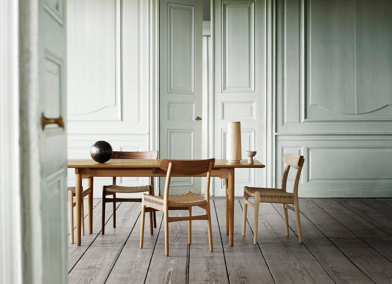 Minimalist dining setup with a solid wood table in a white room and a single chair nearby.