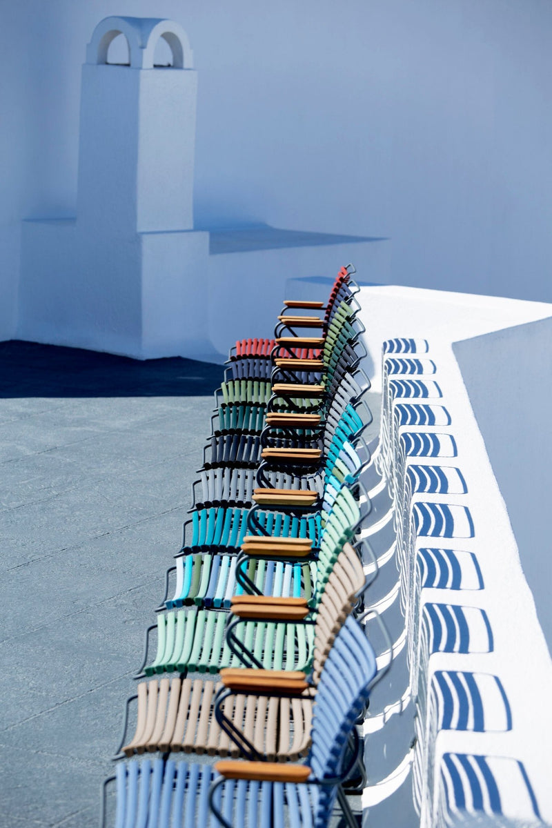 Row of multicolor metal slats forming the chair back and seat, with wooden armrests and metal frame.