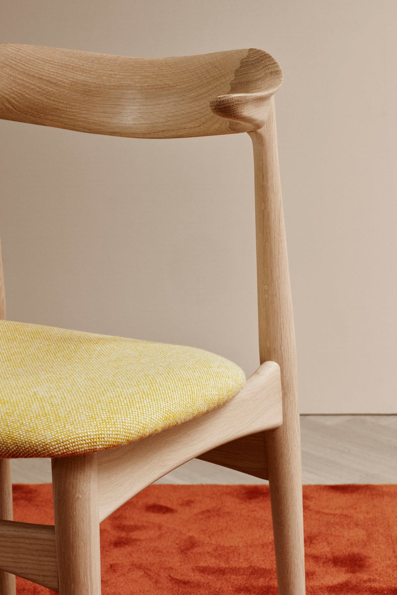 Close-up of wood dining chair showing curved backrest and tapered legs with beige seat cushion.
