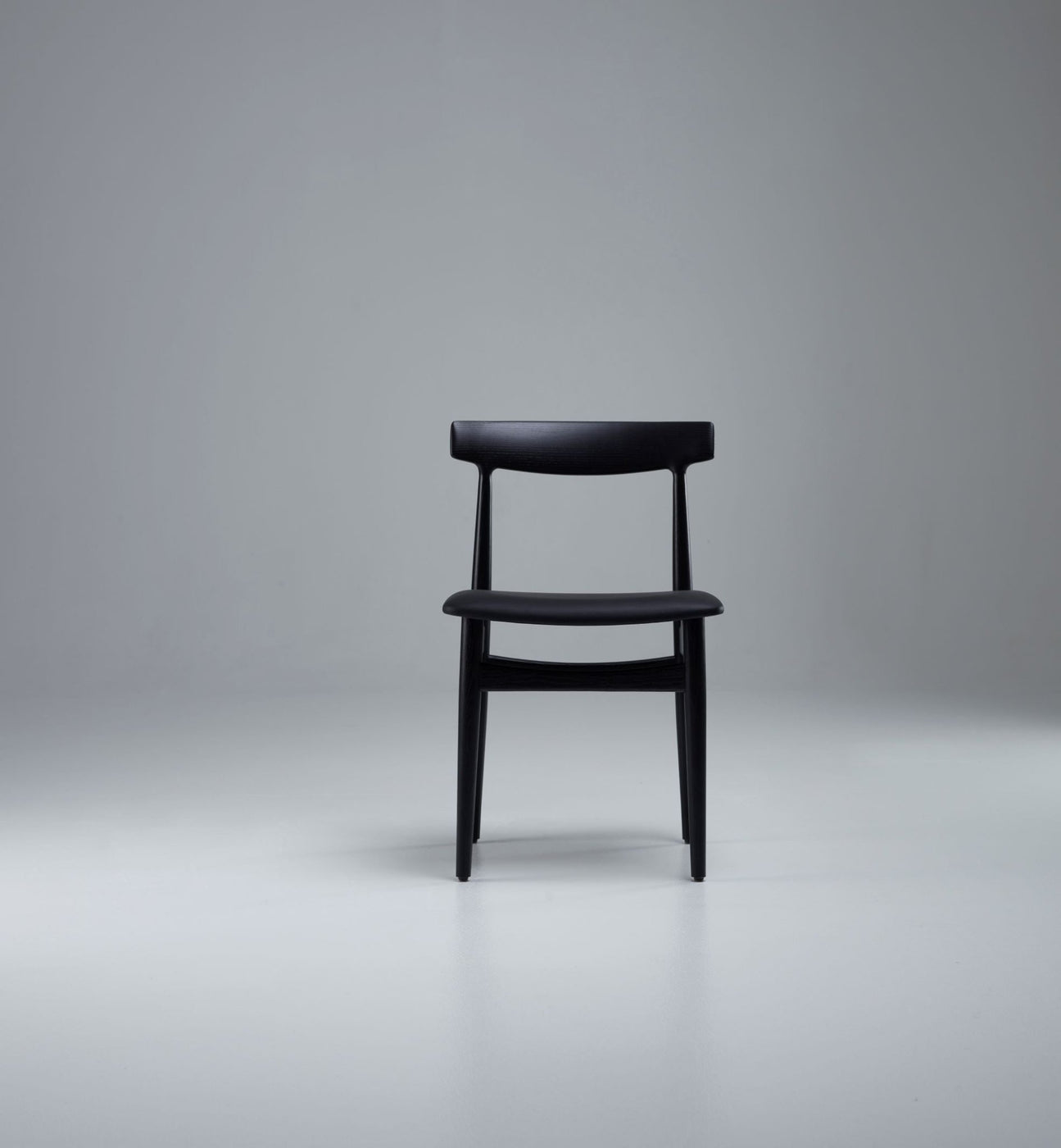 Row of wooden chairs with black seats around a long conference table in a contemporary office space.