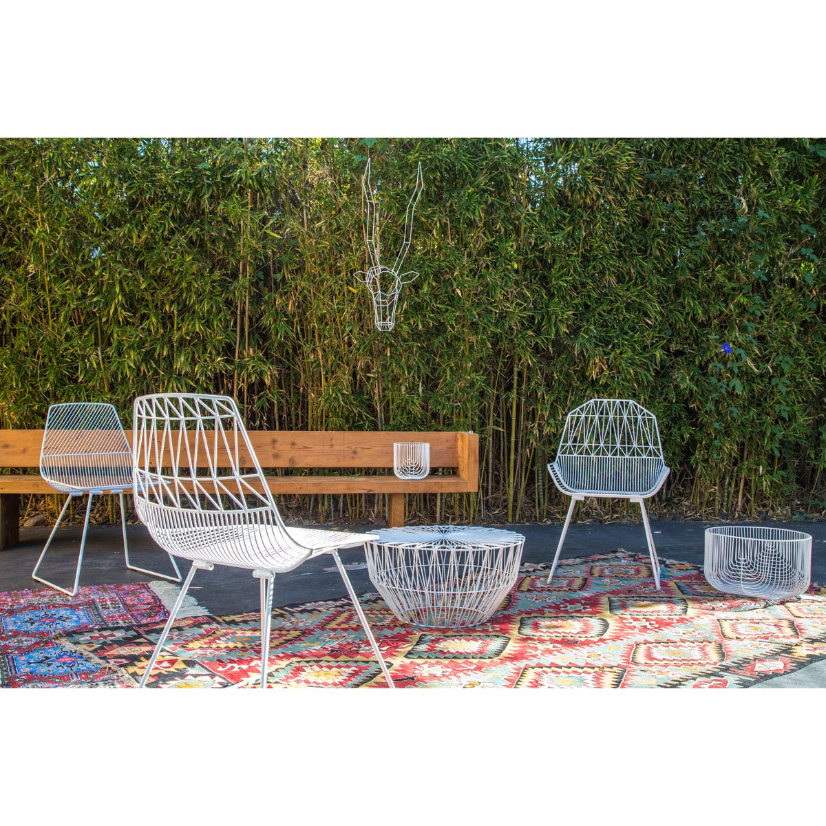 Colorful outdoor wire chairs in a dining setting with teal, orange, and blue chairs around white tables on a patterned rug.